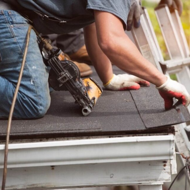 man on roof repairing shingle along gutter